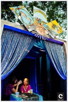 two people sitting at a table in front of a blue canopy with pictures on it