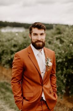 a man with a beard wearing an orange suit and flower in his lapel is posing for the camera