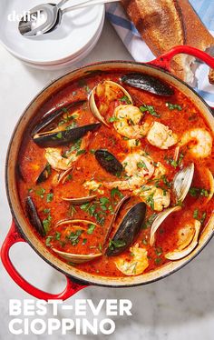 a red pan filled with seafood and clams on top of a table next to bread