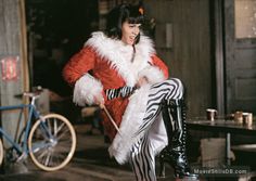 a woman in a red coat and zebra print pants is holding a cane while sitting on a stool