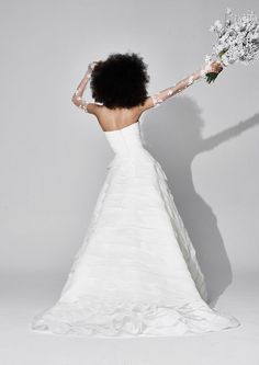 a woman in a white wedding dress holding a bouquet of flowers with her arms outstretched