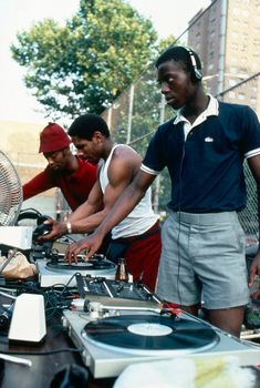 four men are standing around djs at an outdoor event with headphones on their ears