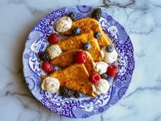 a blue and white plate topped with french toast covered in berries, whipped cream and raspberries