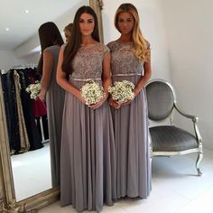 two women standing in front of a mirror wearing long grey dresses with lace detailing on them