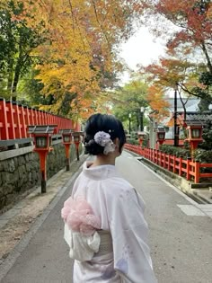 a woman dressed in traditional japanese garb walking down the street with her back to the camera