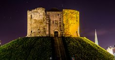 the castle is lit up at night with stars in the sky above it and on top of a grassy hill