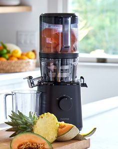 a juicer sitting on top of a wooden cutting board filled with fruits and vegetables