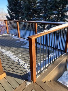 a wooden deck with metal railing and snow on the ground