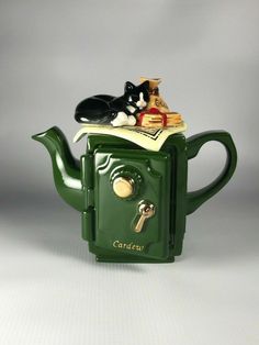 a green teapot with a black and white cat sitting on it's top