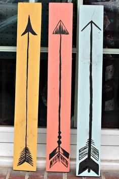 three wooden signs with arrows painted on them sitting in front of a storefront window