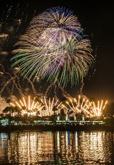 fireworks are lit up in the night sky over water and palm trees with lights reflecting on the water