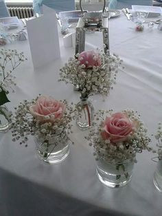 pink roses and baby's breath in small vases on a white table cloth