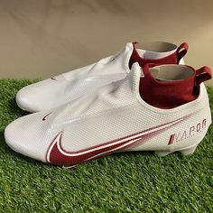 a pair of white and red nike soccer cleats sitting on green grass in front of a wall