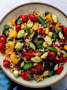 a white bowl filled with couscouse, zucchini and vegetables on top of a blue towel