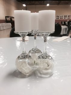 two wine glasses with white flowers and candles on a table in a banquet hall or conference room