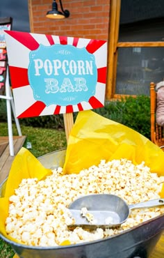 popcorn is sitting in a metal bowl on top of a table with chairs and a sign behind it