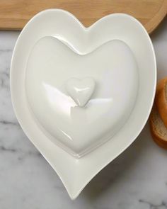 a white heart shaped dish next to two slices of bread