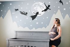 a pregnant woman standing next to a crib in front of a wall with tinkerbells on it