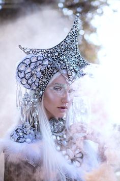 a woman with long white hair wearing a silver headdress and large crystal earrings