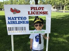 a young boy wearing sunglasses and a pilot license sign stands in front of the grass