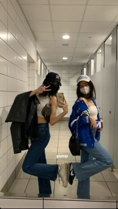 two young women standing in a hallway with masks on their faces and one holding a cell phone to her ear