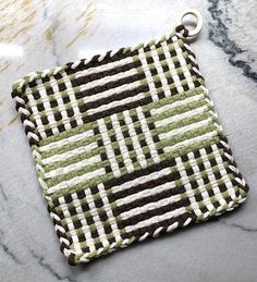 a green and white square shaped bag on a marble surface with a key chain attached to it