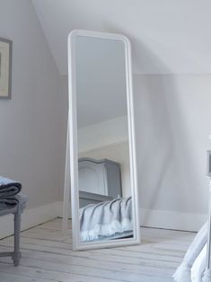 a large white mirror sitting on top of a wooden floor next to a bed in a bedroom