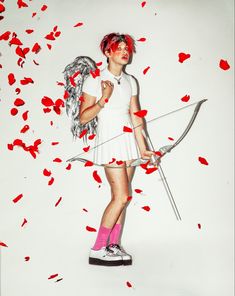 a woman with red hair holding a bow and arrow in front of petals on the ground