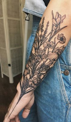 a woman's arm with flowers and leaves tattooed on her left arm, in black ink