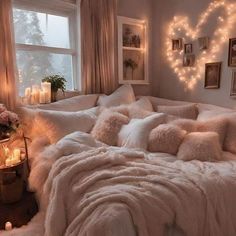 a bed with fluffy blankets and candles in the corner next to a window filled with lights