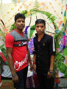 two young men standing next to each other in front of a wall with flowers on it