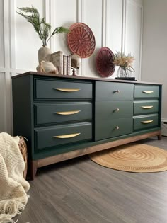 a green dresser with gold handles in a white living room next to a rug and potted plants