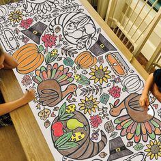 two children sitting at a table with a large coloring book on it's floor