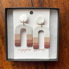 a pair of white and brown earrings in a box on a wooden table with the words copper jones studio written below it