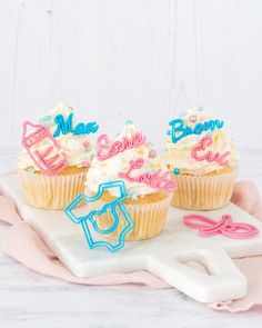 three cupcakes with frosting and decorations on a white tray next to pink napkin