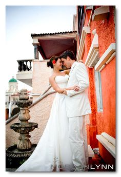 a bride and groom standing next to each other in front of a red building with water fountain