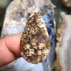 a person holding a piece of crystal in their hand with other rocks behind it and water on the ground