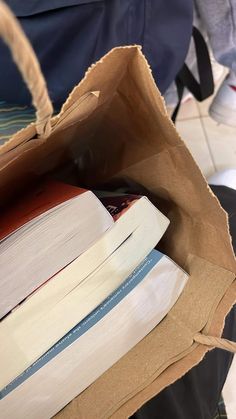 a brown paper bag filled with books sitting on top of a white tile floor next to a pile of books