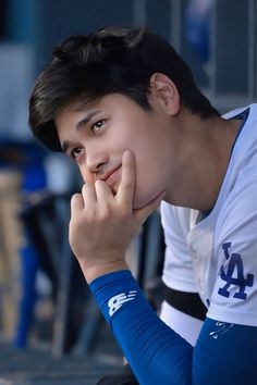 a young man sitting down with his hand on his chin and looking at the camera