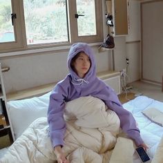 a woman sitting on top of a bed in a purple hoodie and white pants