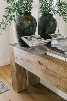 two vases with green plants on top of a wooden table in front of a mirror