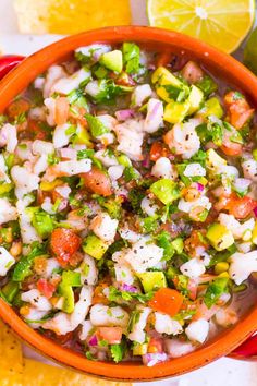 an orange bowl filled with shrimp salad next to sliced lemons and lime wedges