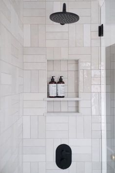 a white tiled shower with black fixtures and shelves above the shower head, along with two soap dispensers