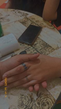 two people sitting at a table with their hands on each other's fingers, one holding the other