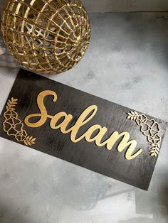 a wooden sign that says salam on it next to a gold ball and vase