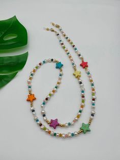 a necklace with multicolored beads and stars on it next to a green leaf