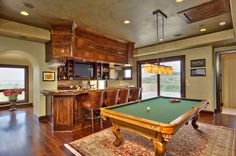 a pool table in the middle of a living room with an entertainment center and bar