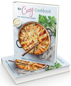 the cozy cookbook is sitting on top of a book with two pizzas in it