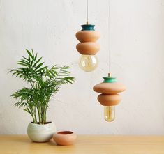 three wooden hanging lights on a table next to a potted plant and an empty vase