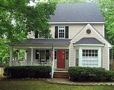 a white house with a red door and black shutters on the front, surrounded by trees